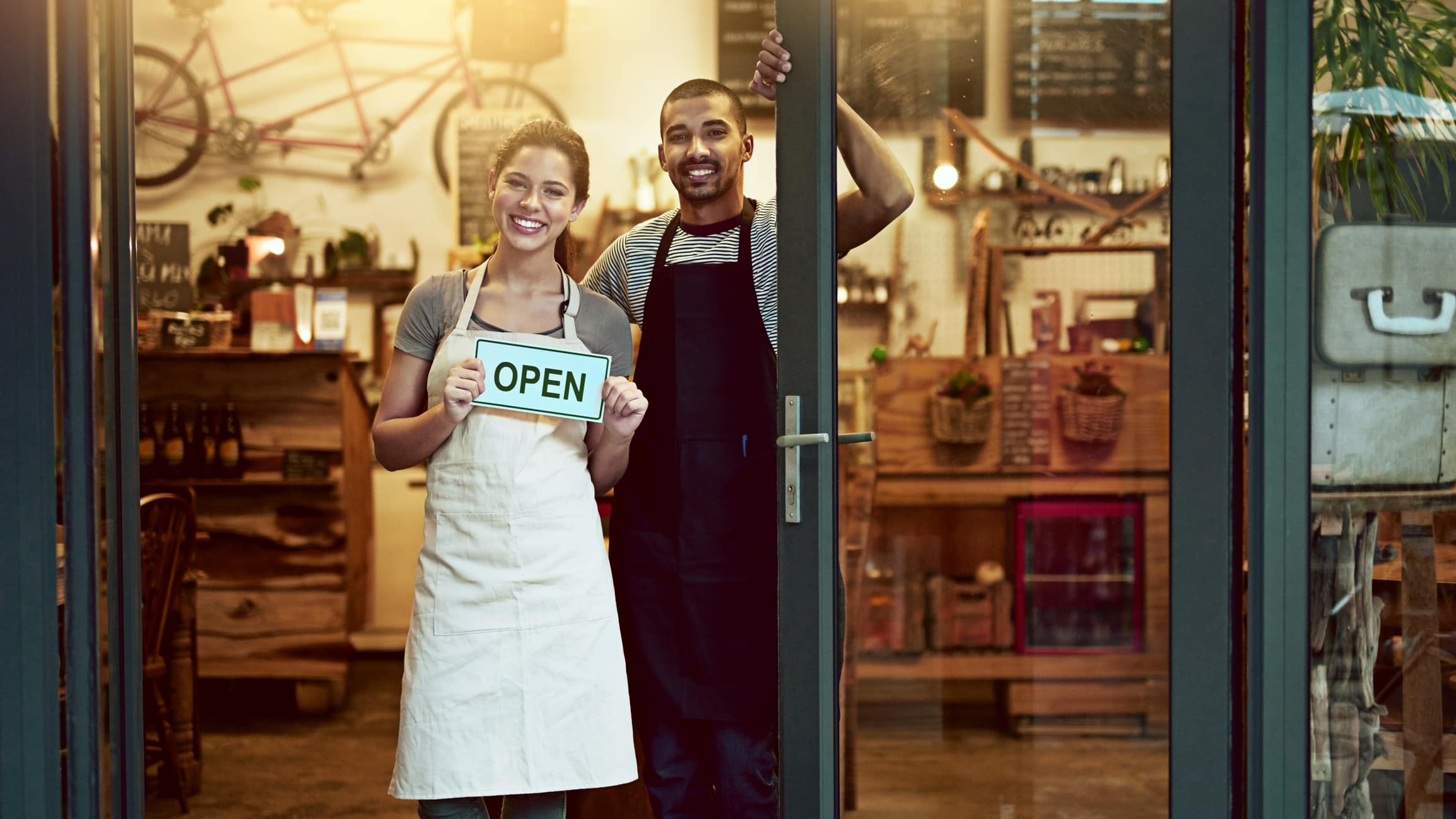 Portrait of a young man and woman holding up an open sign in their store