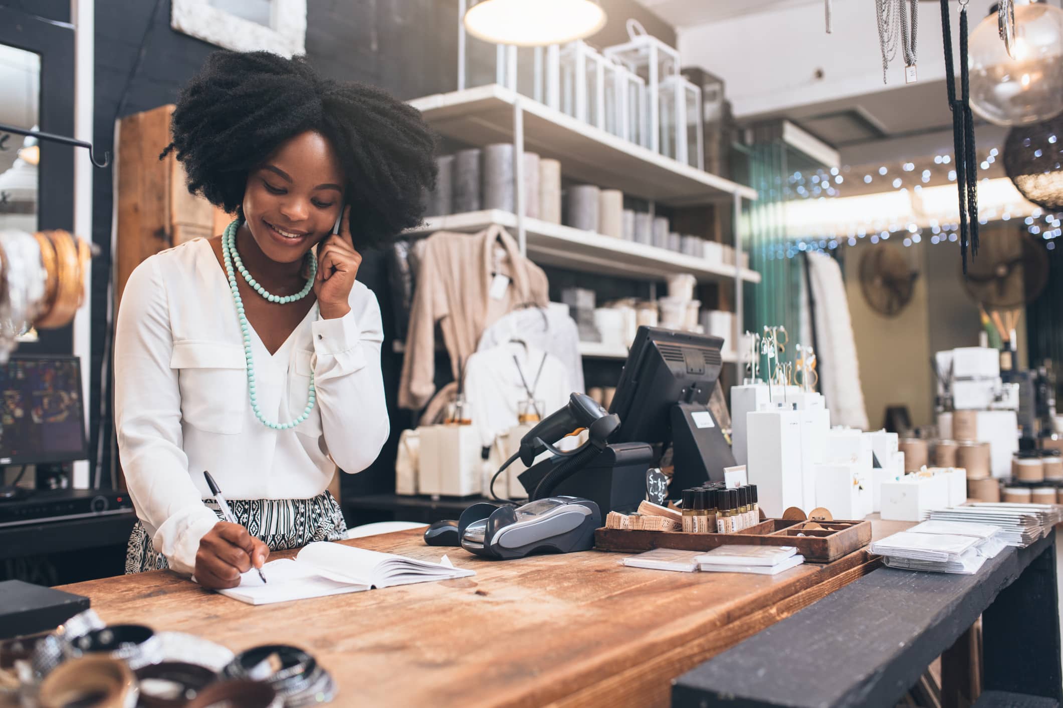 Shot of a happy young shopkeeper using her cellphone while standing behind the counter in her shop